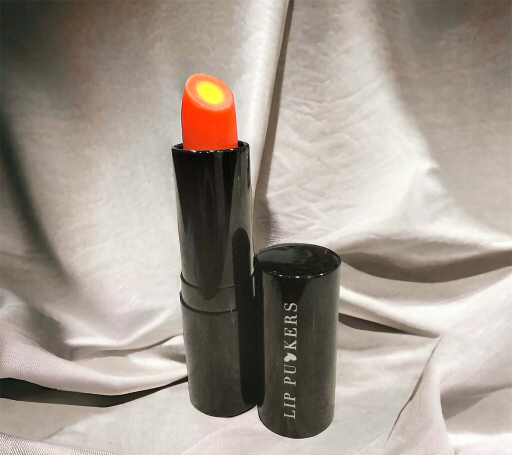 Sunray Vitamin C Lip Treatment Stick with glowing orange balm in black tube labeled Lip Puykers against a soft fabric background